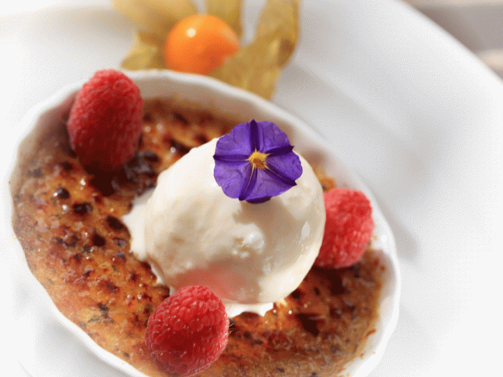 Ein goldbrauner Pancake, garniert mit Joghurt, frischen Himbeeren und einer violetten Blüte.