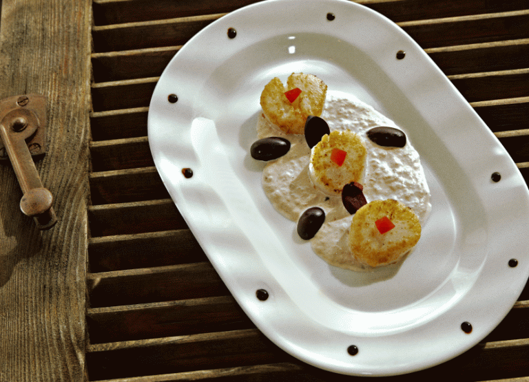 Eine weiße Servierplatte mit mehreren kleinen, goldbraunen Pfannkuchen, angerichtet auf einem dunklen Holzuntergrund.